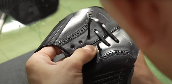Pekerja pabrik sepatu sedang menjahit bagian upper sepatu dari bahan kulit di ruang produksi
